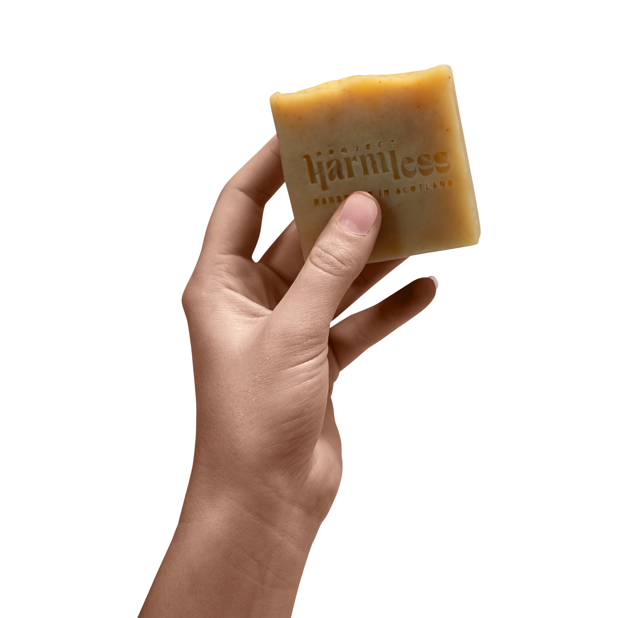 Hand holding Project Harmless soap, embossed with the brand logo and “Handmade in Scotland.” A minimalist product shot highlighting the artisanal craftsmanship of this palm oil-free, organic essential oil-infused soap. Sustainable, plastic-free, and slow-cured for 28 days for a superior lather and nourishment.