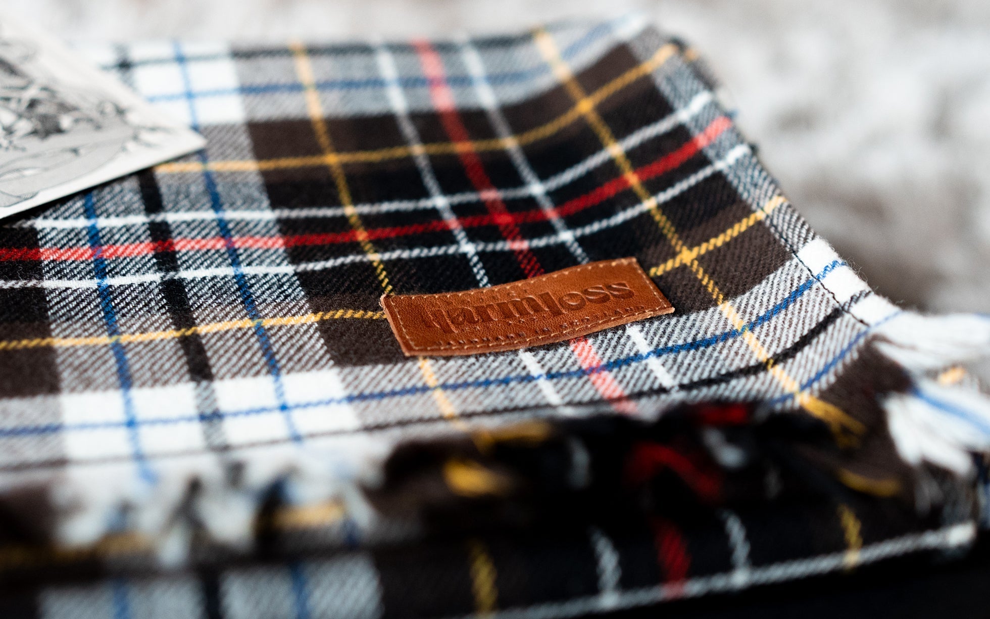 Close-up of a 100% wool tartan scarf by Project Harmless, featuring a leather label and showcasing sustainable Scottish craftsmanship and slow fashion values.