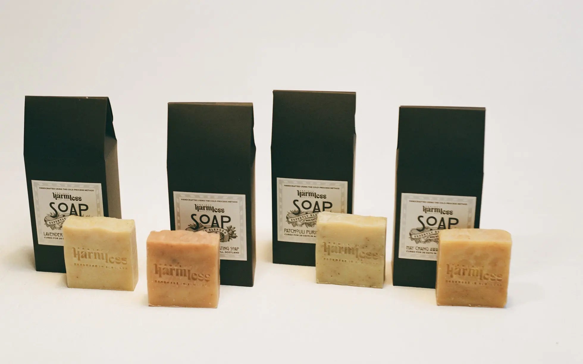 Four handcrafted, palm oil-free soaps from Project Harmless standing upright in front of elegant, eco-friendly packaging. Made with organic essential oils and Scottish soft water for a luxurious, sustainable skincare experience.