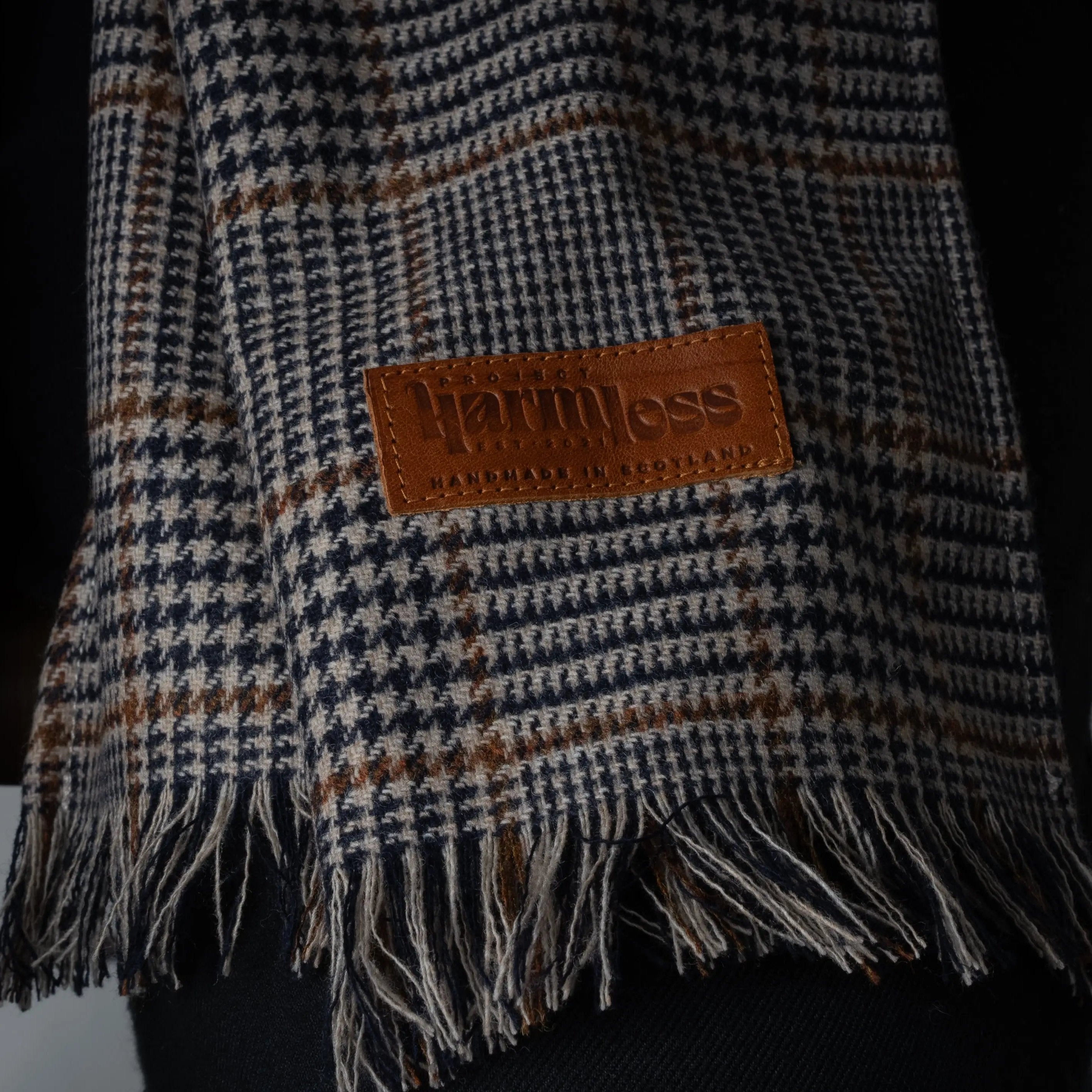 Atelier District Check Merino Scarf by Project Harmless – A sustainably woven, exceptionally soft scarf featuring a timeless district check pattern. Showcased with the Project Harmless upcycled leather logo patch, hand-stamped and detailed with ‘Handmade in Scotland’ text, highlighting eco-luxury and ethical craftsmanship.