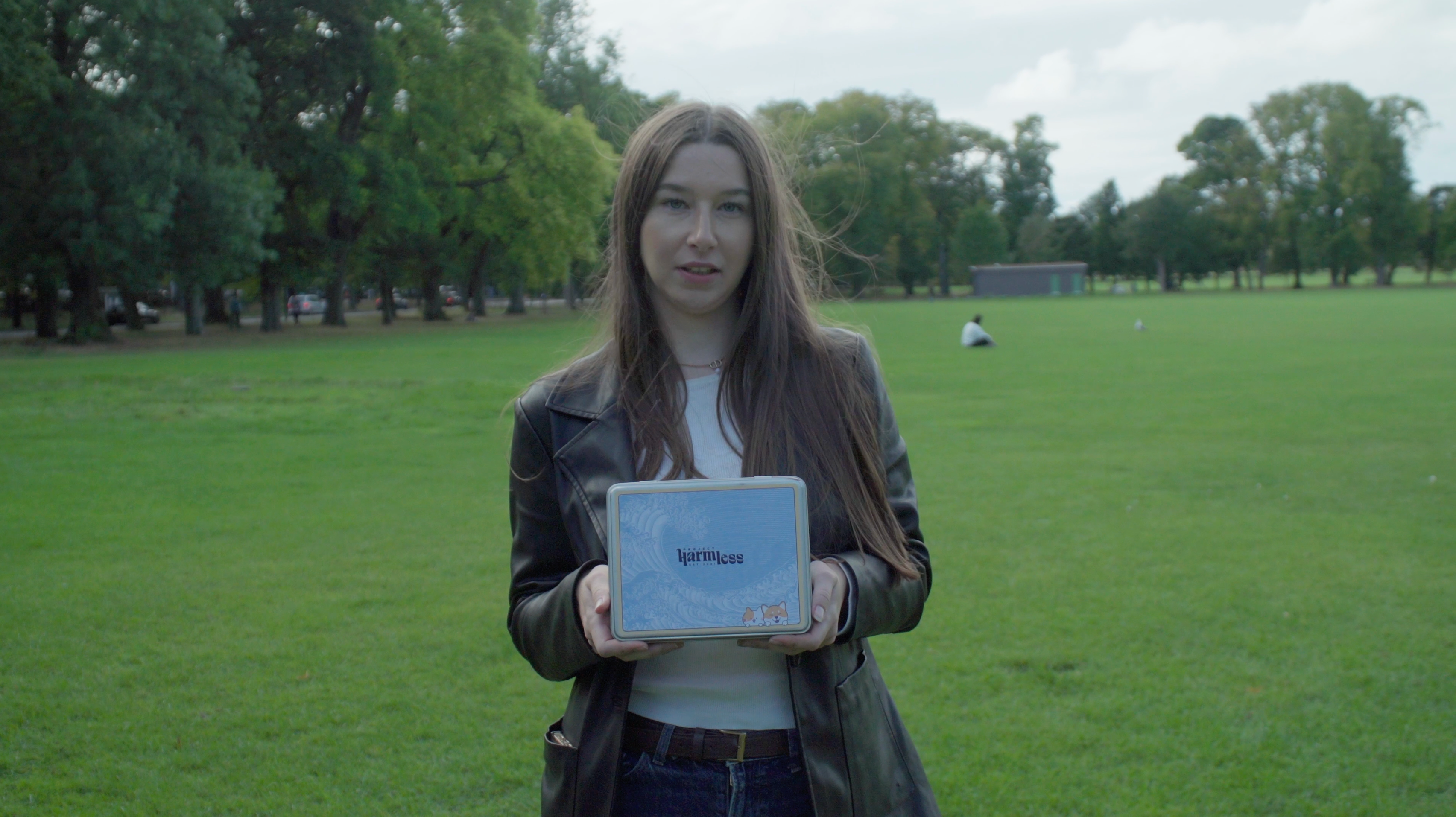 Project Harmless team member holding an eco-friendly tin of Project Harmless biodegradable dog poop bags in a green park, promoting sustainable pet waste solutions.