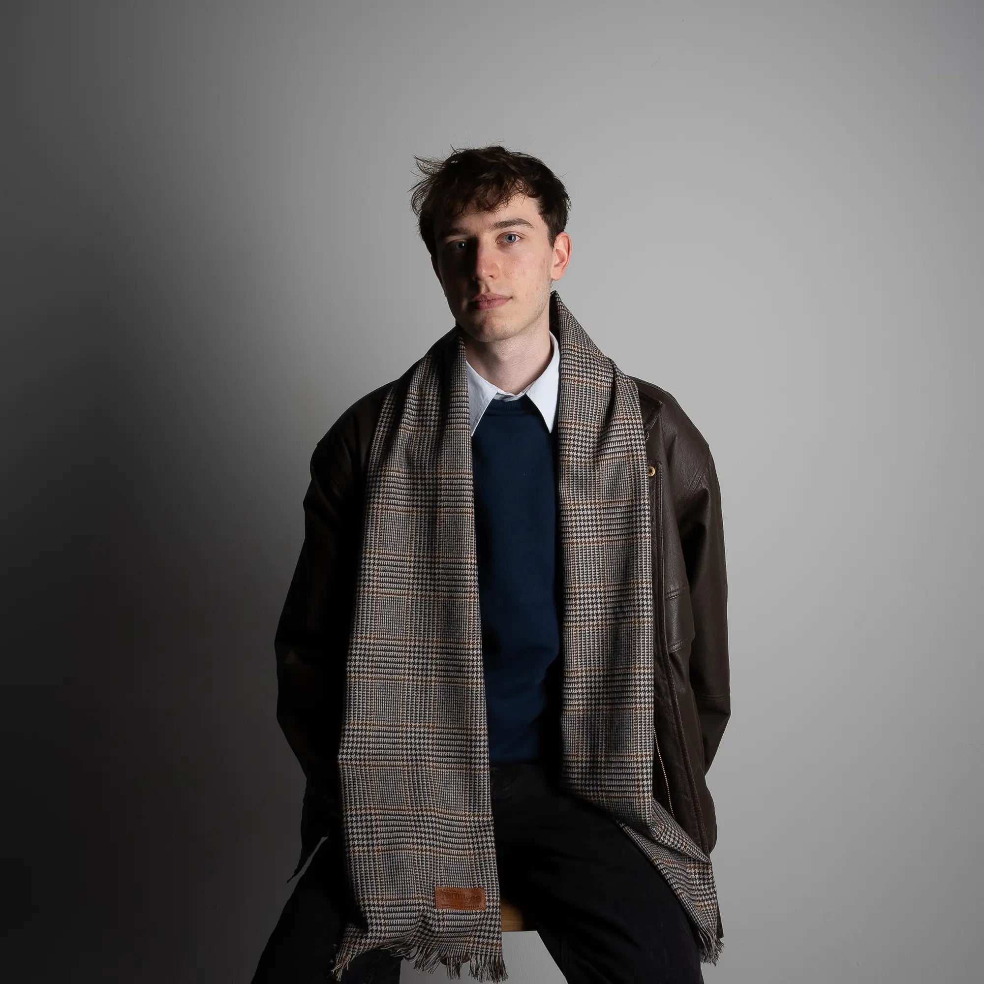 Male model wearing the Project Harmless Atelier District Check Merino Scarf in a studio in Scotland, styled with tailored outerwear, highlighting its classic design and softness.