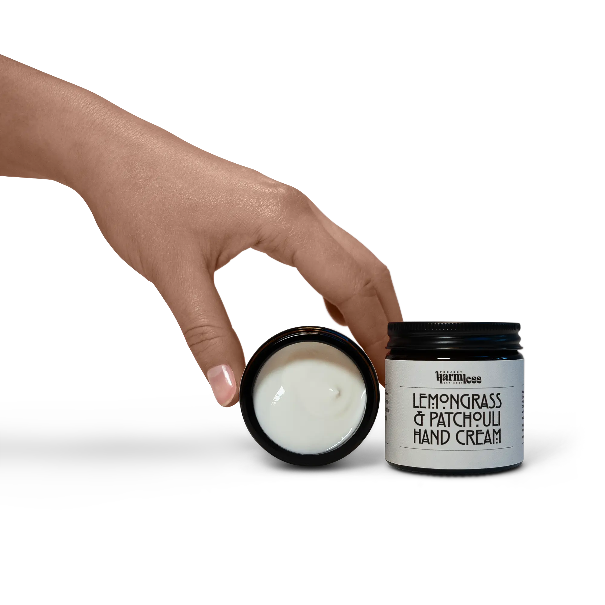 Hand holding the Harmless Apothecary by Project Harmless Lemongrass & Patchouli Hand Cream jar, highlighting its creamy texture.