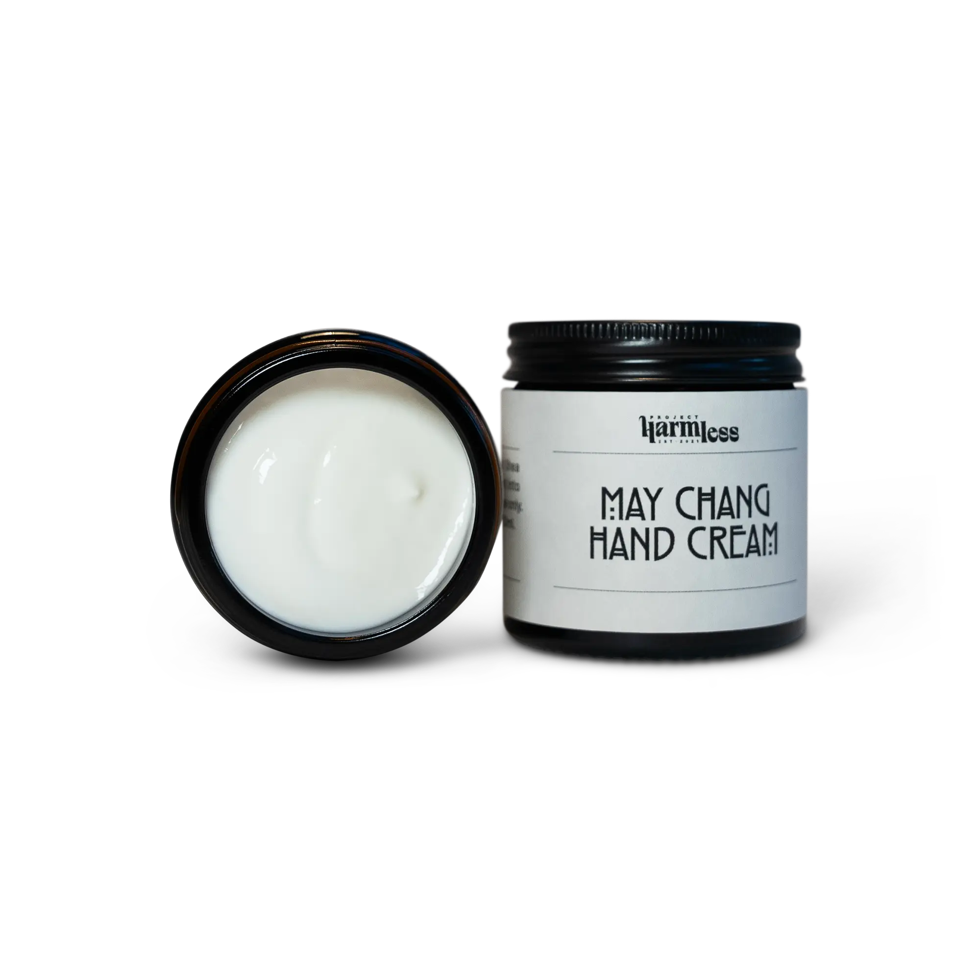 May Chang hand cream by Project Harmless, displayed next to an open premium black glass jar with an aluminum cap and a label made from premium textile, showcasing the rich texture of the cream. Part of Harmless Apothecary, crafted in small batches with organic essential oils.