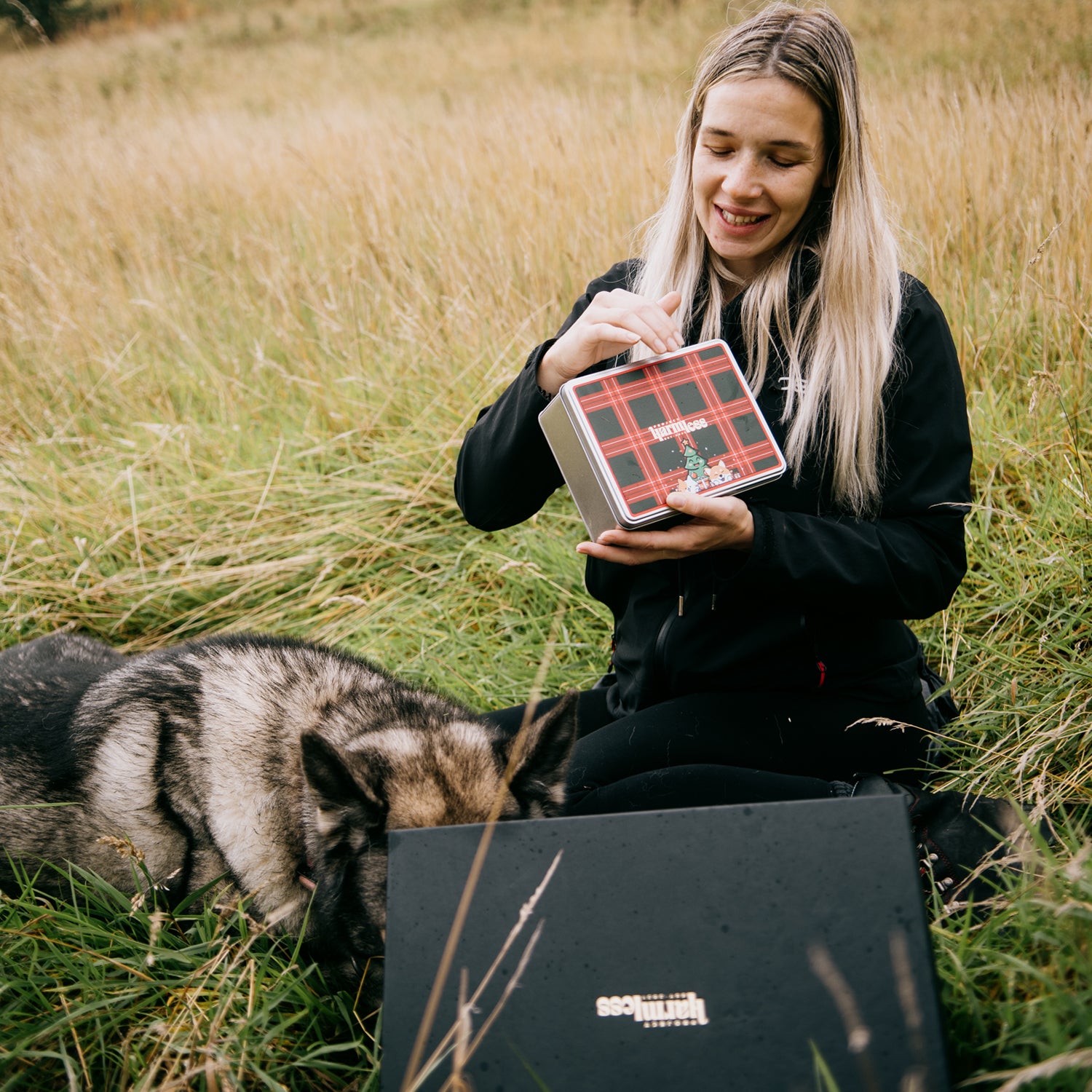 Luisa Hendry (@scottishgeologist)
in the outdoors holding a Project Harmless festive dog gift tin and black gift box in the Scottish Highlands, sustainable Christmas gift bundle for dog owners.