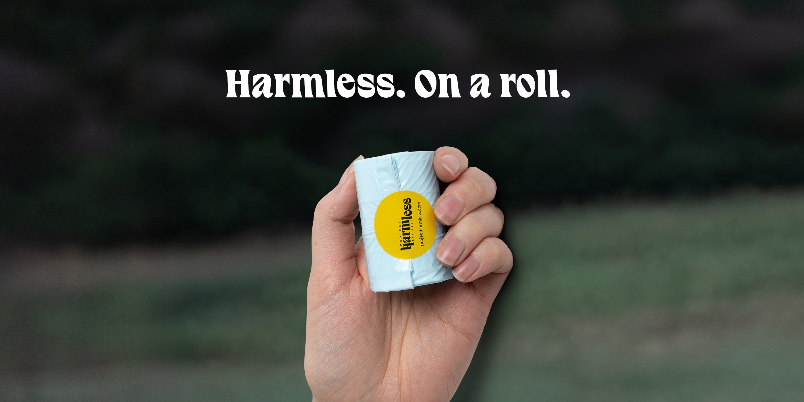 Hand holding a roll of Harmless dissolvable dog poop bags, with the words "Harmless. On a roll." overlaid