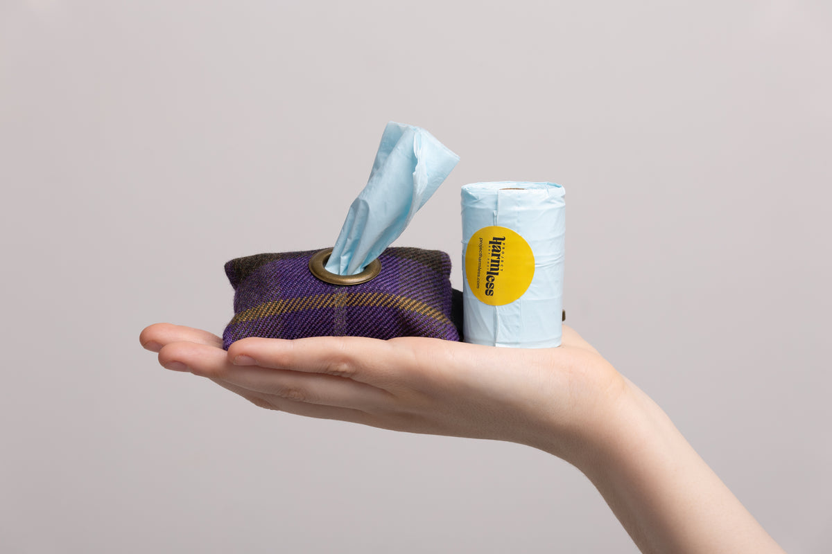 Purple tartan dog poo bag holder with brass eyelet, handmade in Scotland, shown with a roll of Harmless Poop Bags