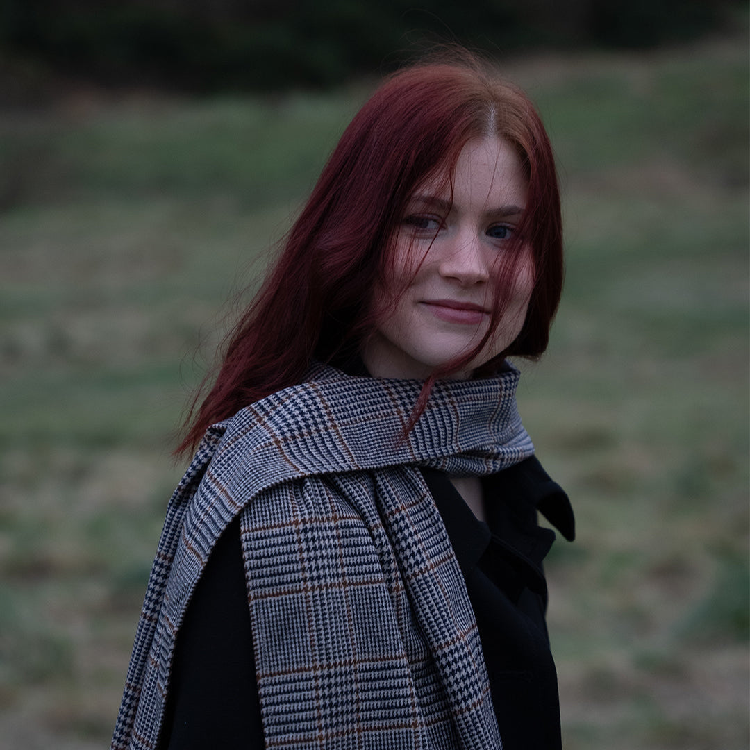 Reflective model wearing the Harmless Atelier District Check Merino Wool Scarf in Holyrood Park, Edinburgh. The scarf’s soft Merino wool and timeless elegance highlight Project Harmless’s commitment to sustainability and Scottish craftsmanship.