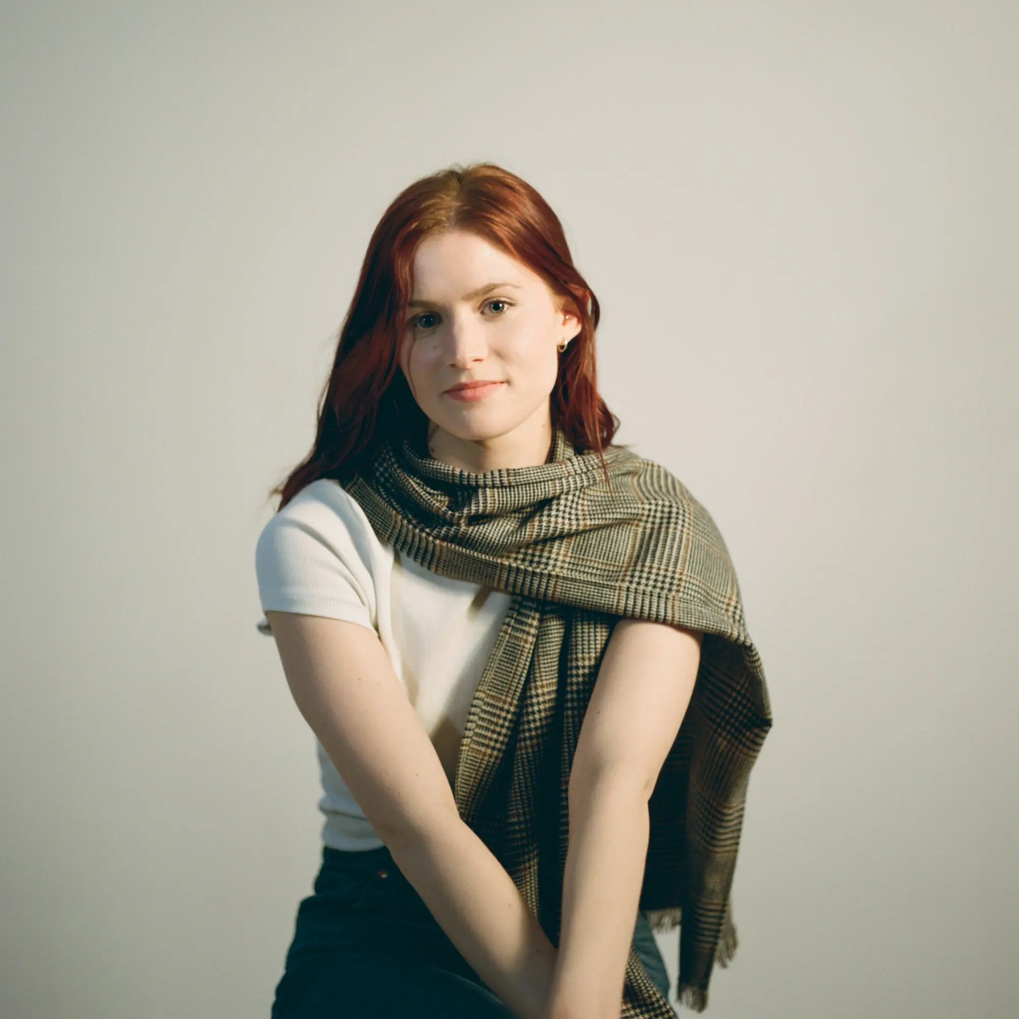 Model wearing the Harmless Atelier District Check Scarf by Project Harmless, a luxurious Scottish-made wool scarf, in a studio setting. Handcrafted in the Scottish Borders from rare revitalized fabric, this limited-edition sustainable fashion accessory embodies heritage craftsmanship with modern design. A timeless statement piece for those who value ethical fashion, Scottish textile artistry, and eco-conscious luxury.