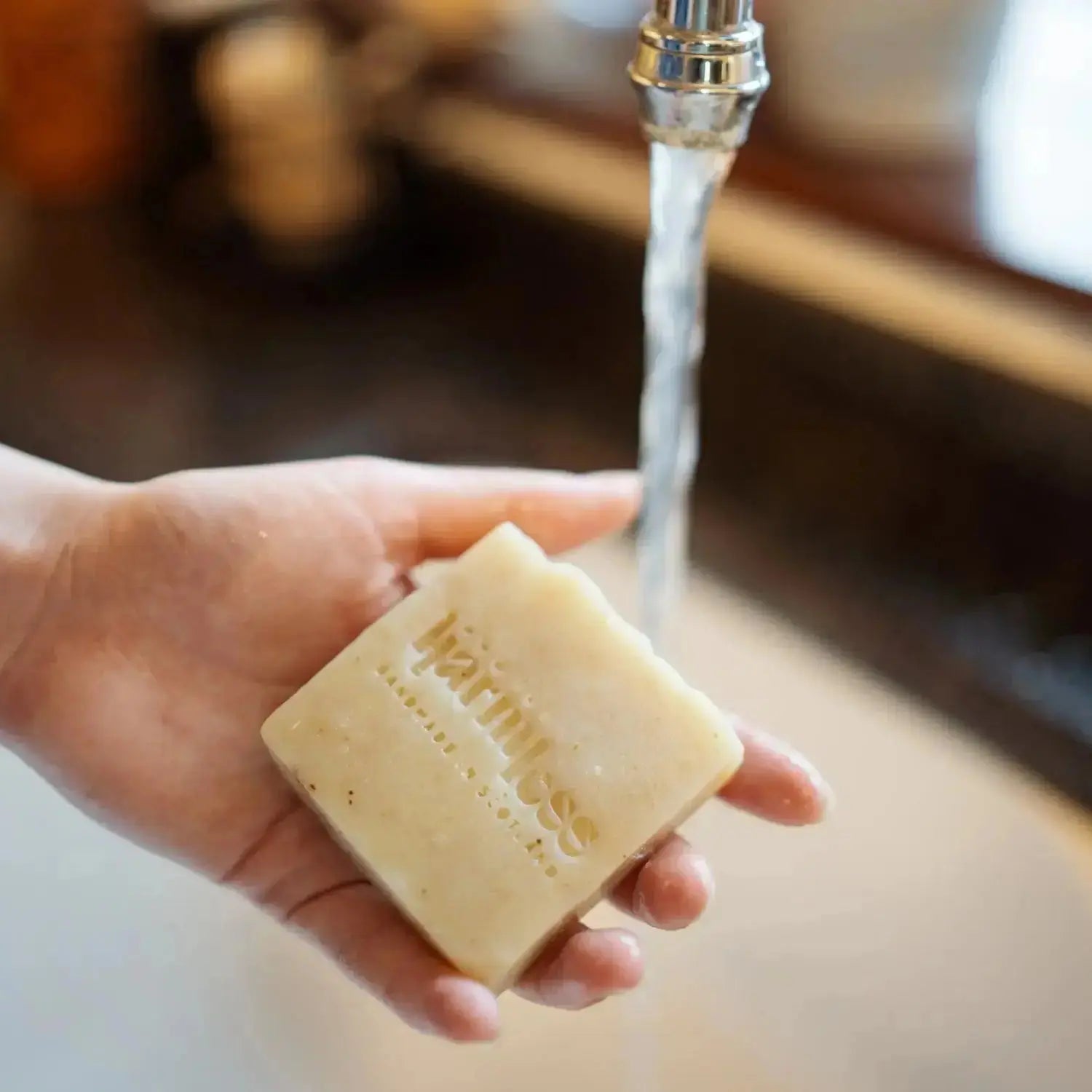 A hand holding a single handcrafted soap from Harmless Apothecary, made in Scotland using the traditional cold-process method. Infused with organic essential oils and enriched with shea butter, olive oil, and pure Scottish water from Argyll and Bute. Palm oil-free and plastic-free, designed for a nourishing and indulgent cleansing experience.