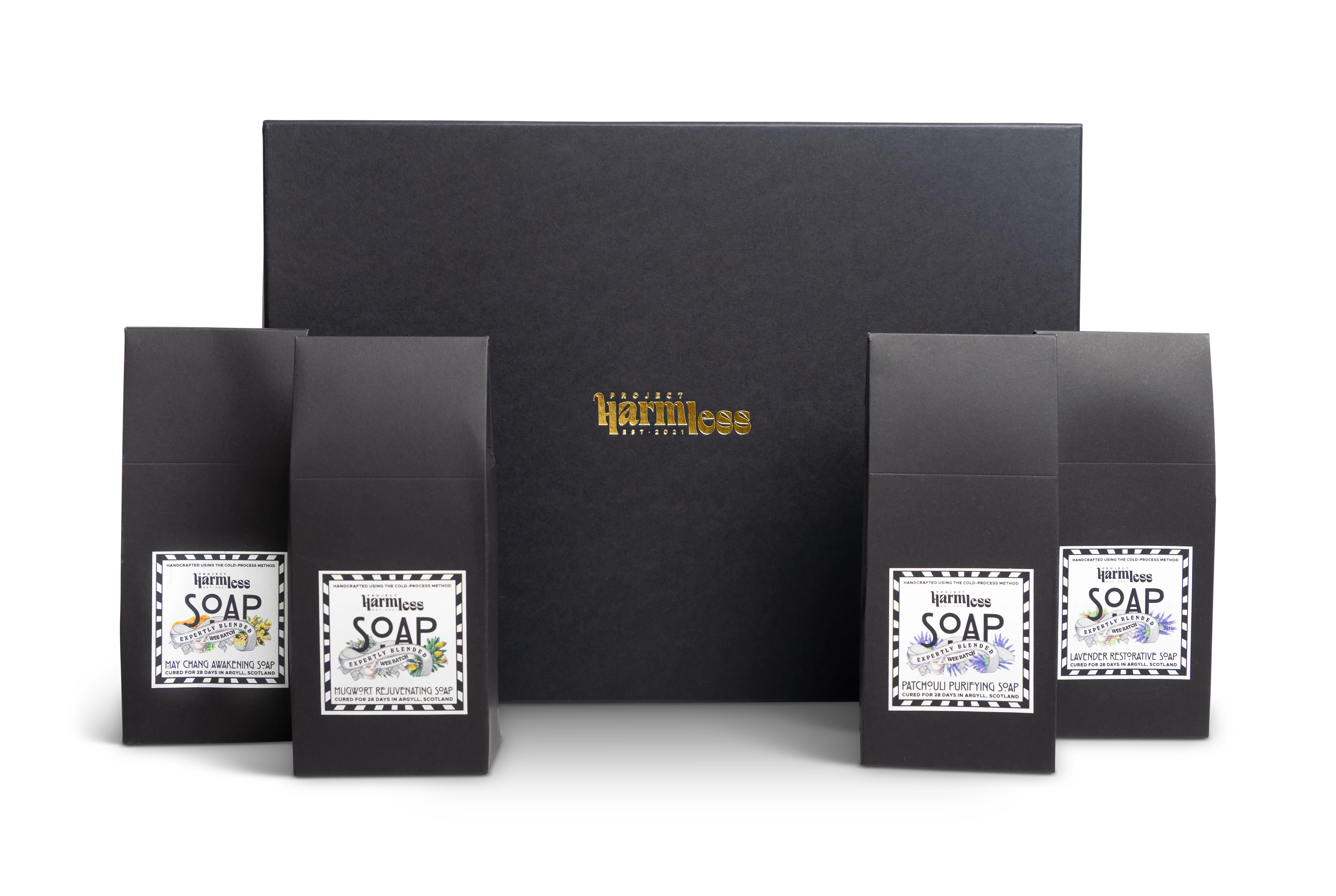 Set of 4 soap packaging in front of a gift box with Project Harmless branding